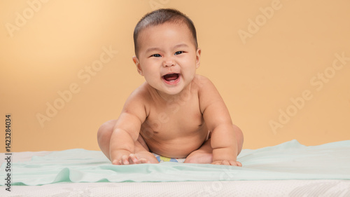 Obraz na płótnie Adorable Asian baby wearing only a diaper, sitting and smiling brightly on a soft mint-colored sheet with a beige studio background, showing joyful and playful expression w salonie