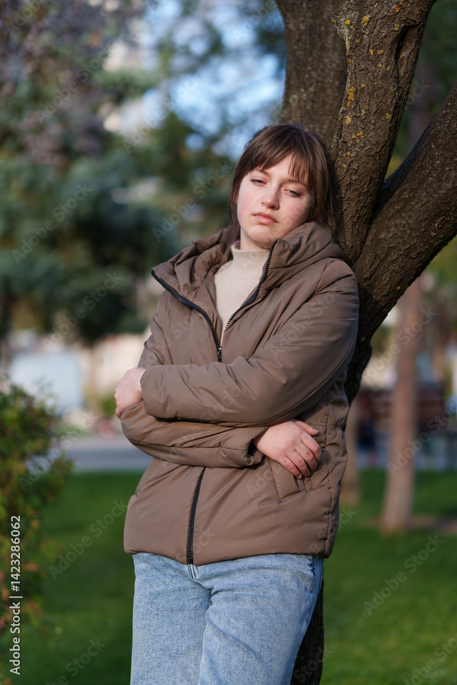 portrait of a teenage girl in a spring park, stands leaning against a tree portrait of a teenage girl in a spring park, stands leaning against a tree