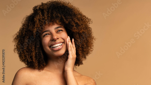 Fotografija Black woman with curly hair smiling in front of beige background - African femal