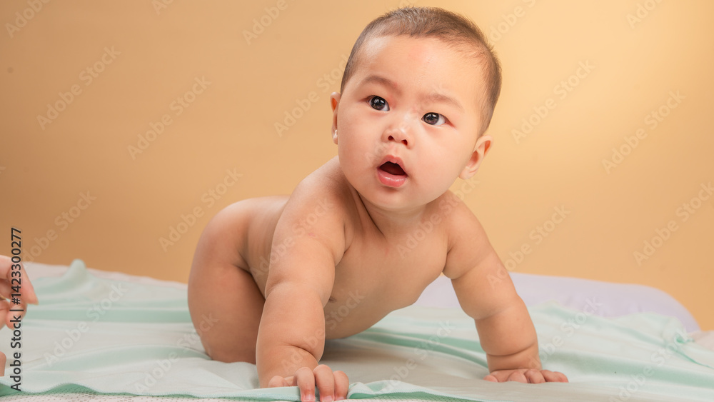 Asian baby crawling on a mint-colored blanket with curious expression, eyes wide open, set against a soft beige background in a cozy indoor studio