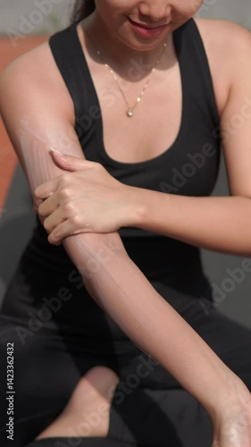 Young Asian woman applying moisturizing sunscreen lotion on face and body before exercising outdoor.
