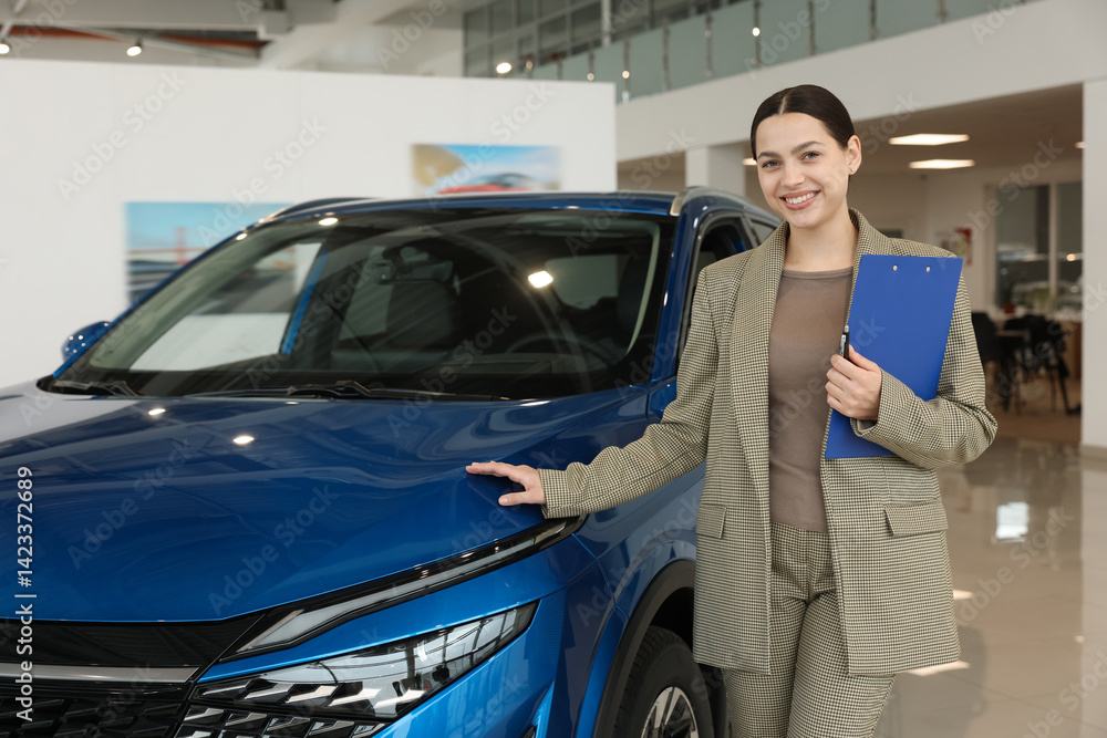 Happy saleswoman with clipboard near new blue car in salon Happy saleswoman with clipboard near new blue car in salon