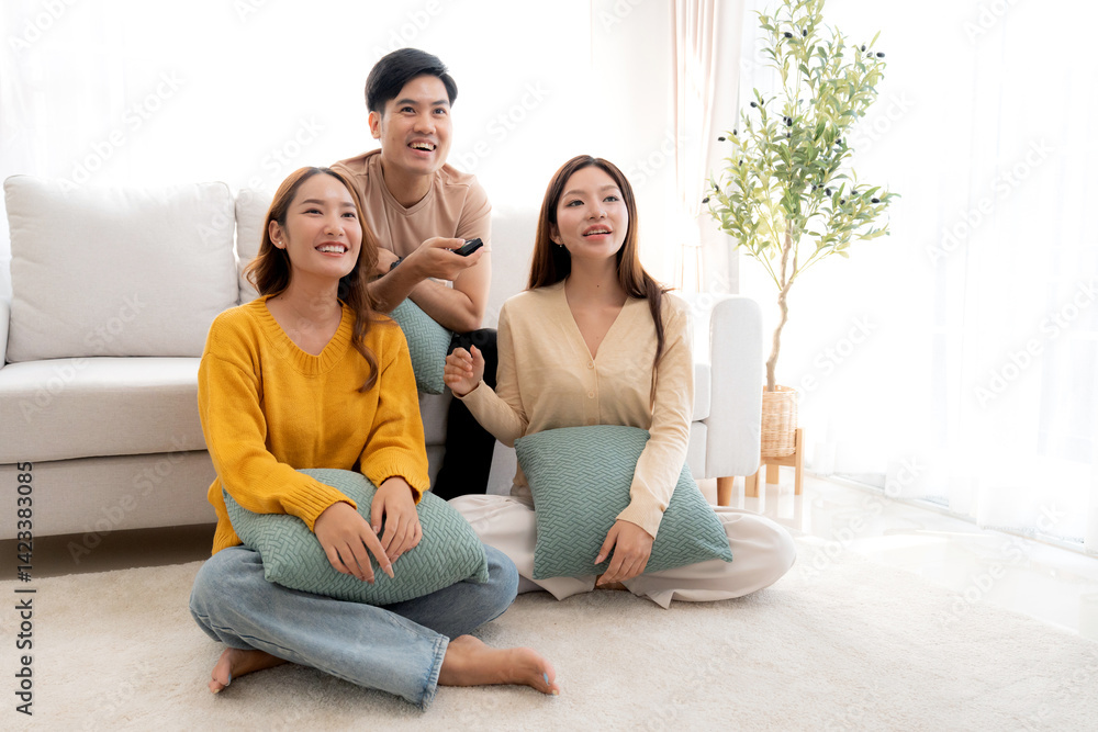 Obraz premium Group young asian friends watching TV together in a cozy living room at home with happy, laughing and enjoying sitting on sofa for watching television with relax, lifestyle and entertainment.