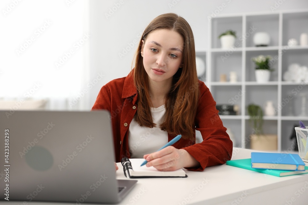 Teenage girl doing homework with laptop at table indoors Teenage girl doing homework with laptop at table indoors