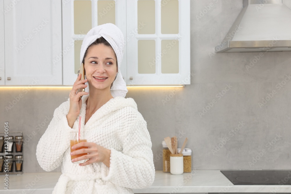 Beautiful woman with glass of juice talking on smartphone after spa procedure in kitchen, space for text Beautiful woman with glass of juice talking on smartphone after spa procedure in kitchen, space for text
