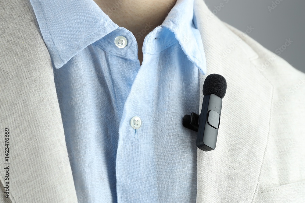 Man with lavalier microphone attached to his suit on grey background, closeup