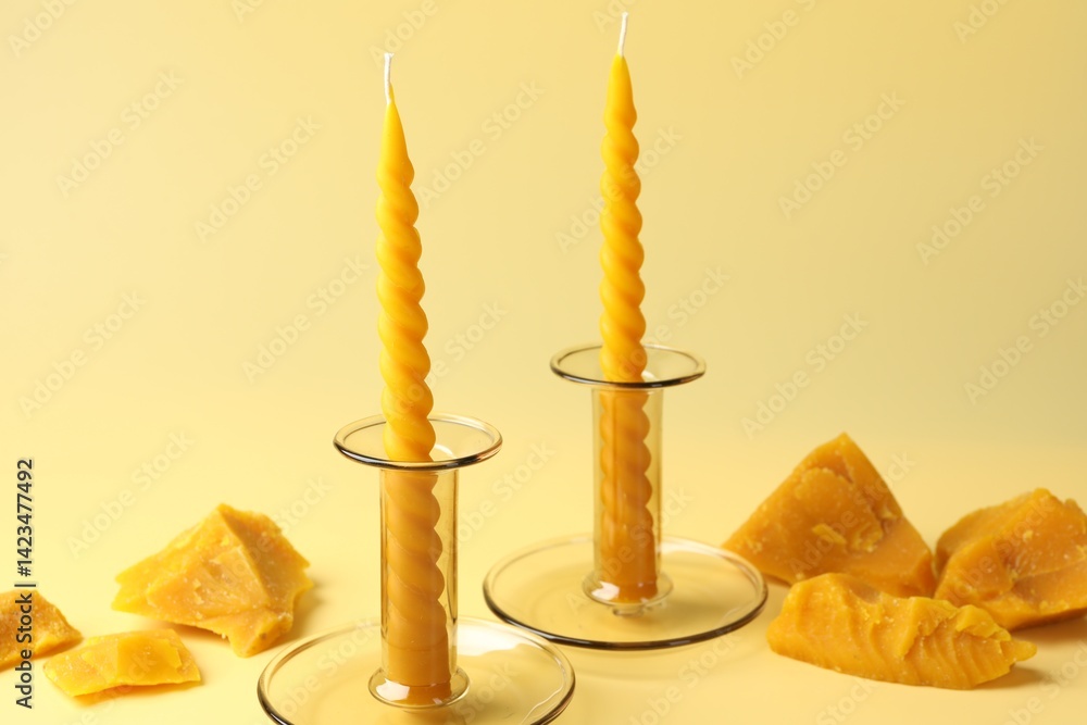Beeswax candles in candlesticks and wax pieces on beige background, closeup