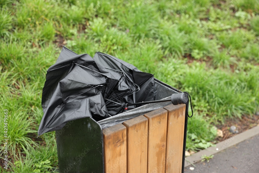 Broken black umbrella in garbage bin outdoors