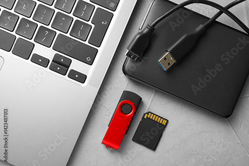 Flash drive, SD memory card, external hard disk and laptop on light grey table, flat lay