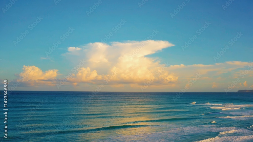 Sunlit beach with ocean waves and light cloud cover at sunset.