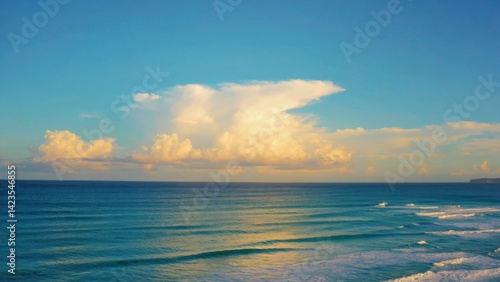 Obraz na płótnie Sunlit beach with ocean waves and light cloud cover at sunset. w salonie