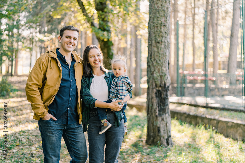 Dad and mom with a little girl in her arms stand among the trees in the forest Dad and mom with a little girl in her arms stand among the trees in the forest