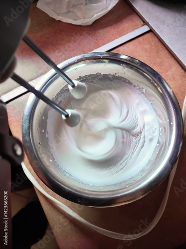 two hand mixer whisks in the process of whipping fresh white cream in a mixing bowl