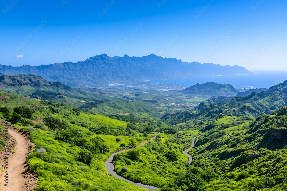 Fototapeta premium Panoramic view of a winding road through lush green mountains and valleys, leading to a distant ocean under a clear blue sky