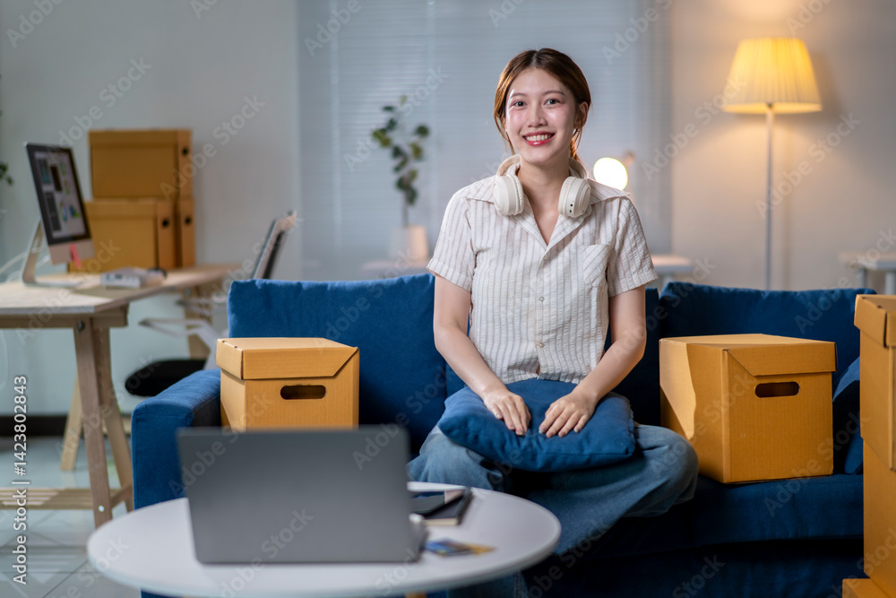 A woman is sitting on a blue couch in a room with boxes and a laptop A woman is sitting on a blue couch in a room with boxes and a laptop