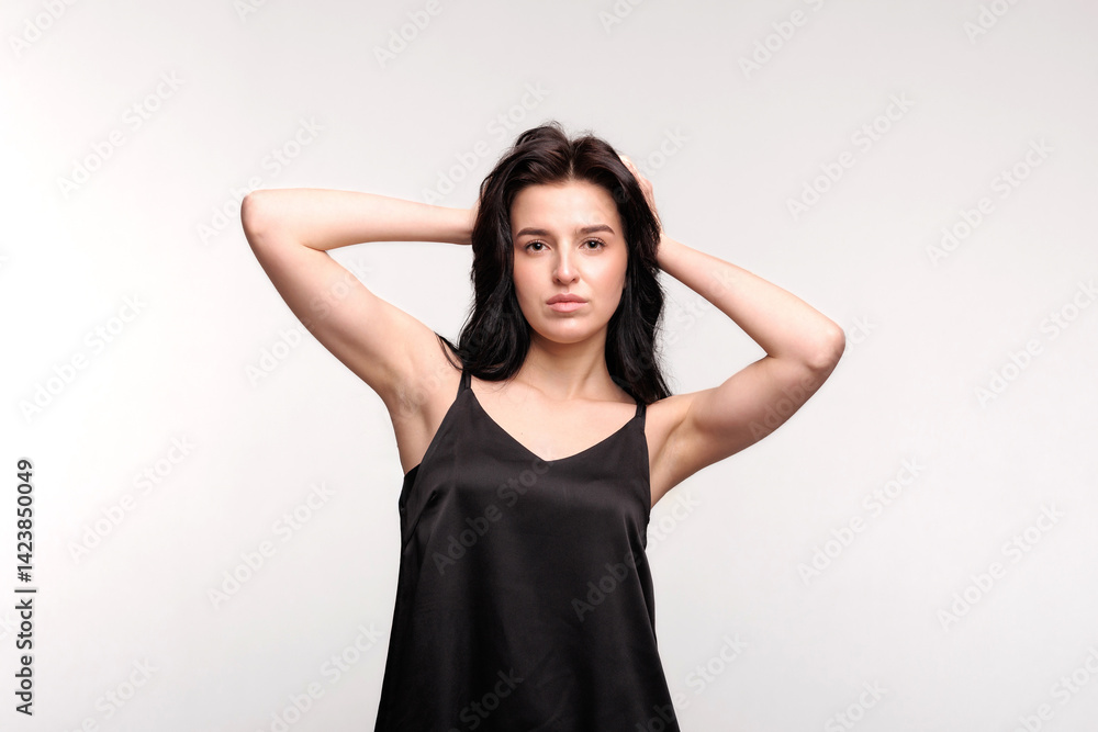 Woman poses confidently with hands in hair, showcasing fashion and beauty in a minimalist studio setting Woman poses confidently with hands in hair, showcasing fashion and beauty in a minimalist studio setting