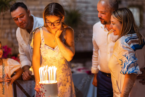 A young girl makes a wish and looks at the birthday cake. A cute teenager in an elegant dress blows out candles on her birthday.