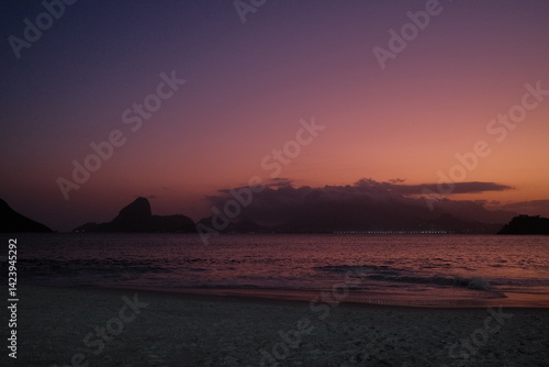 Foto Pôr do sol vibrante na Praia de Icaraí, em Niterói, com vista para o Pão de Açúcar, Baía de Guanabara e o skyline do Rio de Janeiro sob tons de rosa, roxo e laranja