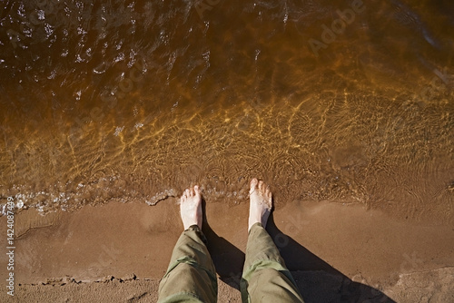 Human feet on sand near water, looking down