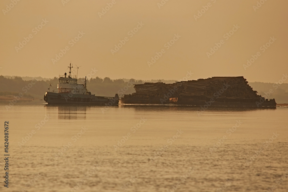 Obraz premium Tugboat and cargo barge carrying timber along river at sunset, close up