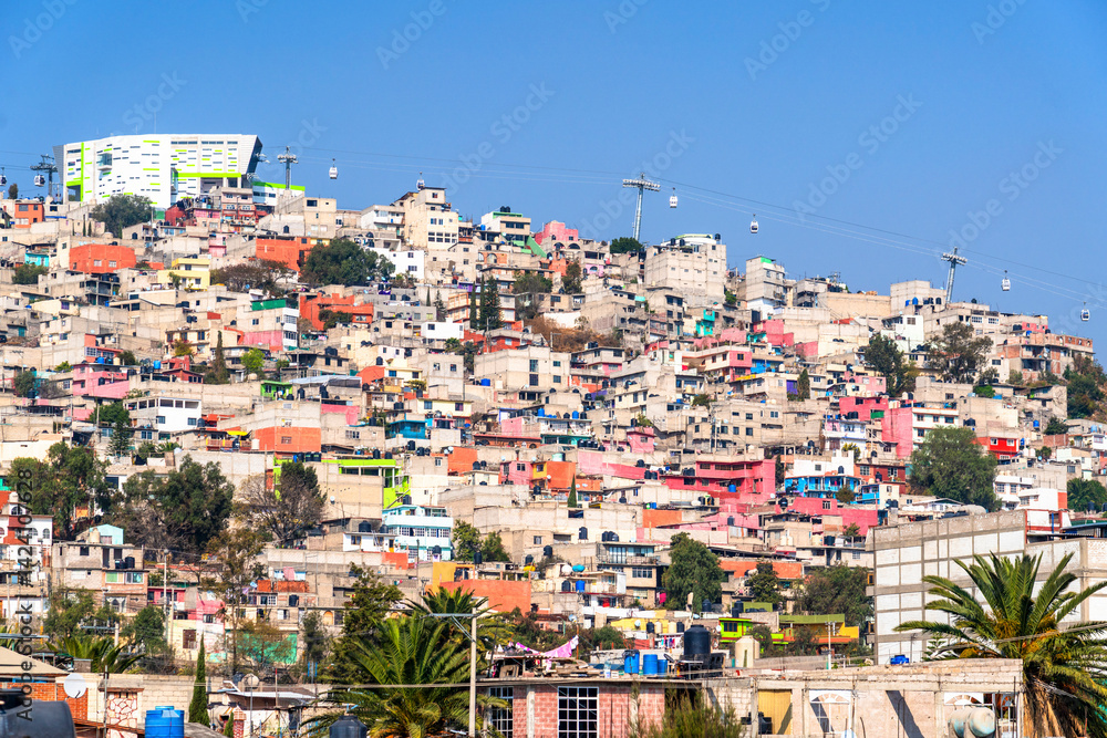 A vibrant hillside community in Mexico City is dotted with colorful homes and connected by the Mexicable cable cars gliding above.