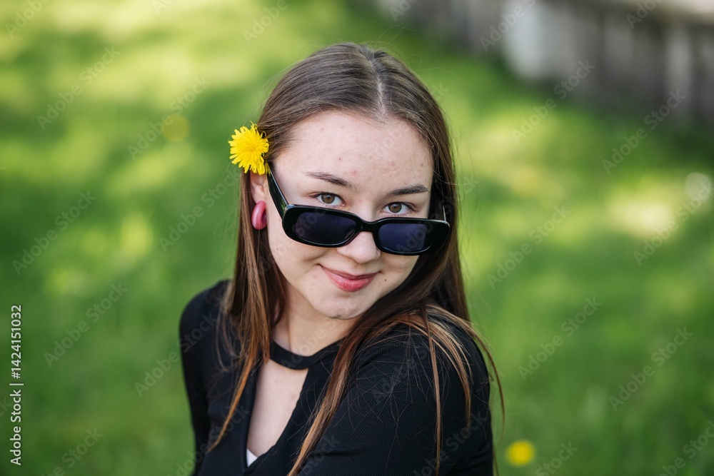 High school student taking a break with a dandelion behind her ear and sunglasses, smiling for a portrait High school student taking a break with a dandelion behind her ear and sunglasses, smiling for a portrait