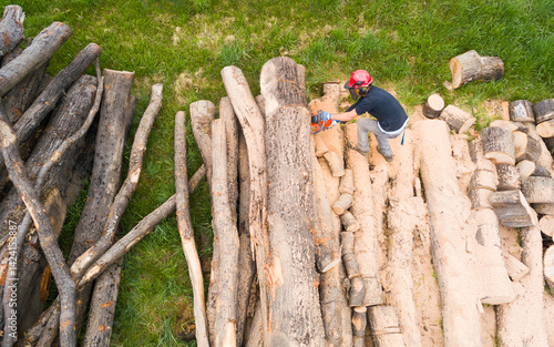 Lumberjack with a chainsaw cutting trees in the forest. Preparing firewood for winter. Top down view. Aerial view from drone
