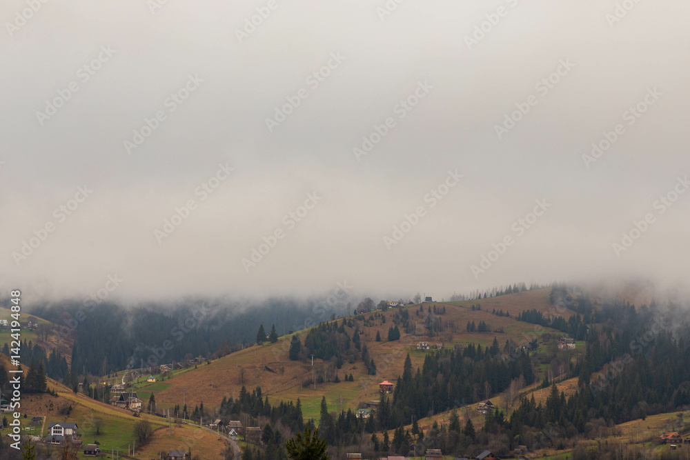Fototapeta premium early morning in a mountain village, clouds slowly rising upwards, revealing a view of the surrounding slopes
