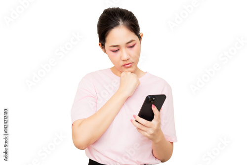 A young woman in a pink shirt is thoughtfully looking at her smartphone.