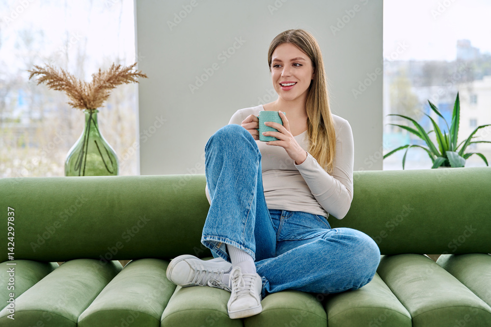 Portrait of relaxed beautiful young woman sitting at home on sofa with cup