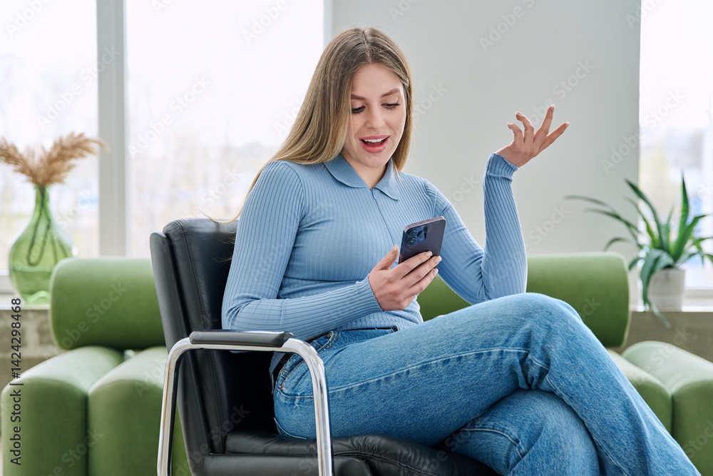 Young woman sitting at home in chair using smartphone