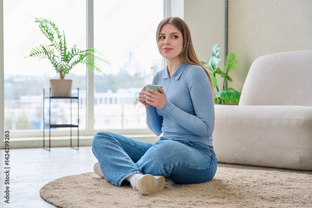 Portrait of relaxed beautiful young woman sitting at home on floor with cup tea