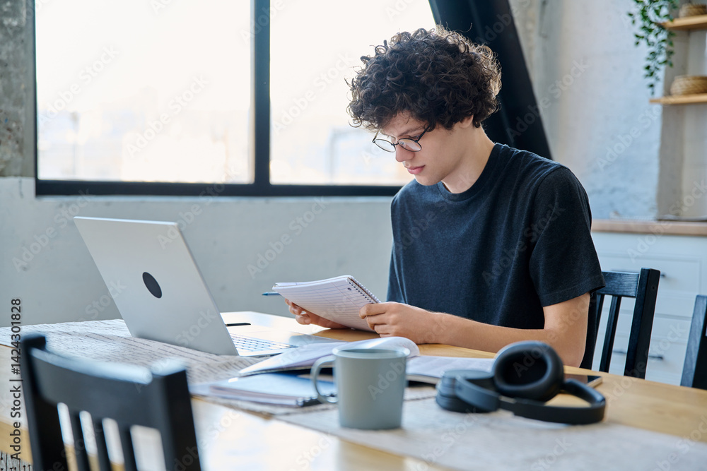 Serious guy studying with laptop textbooks sitting at home at table Serious guy studying with laptop textbooks sitting at home at table