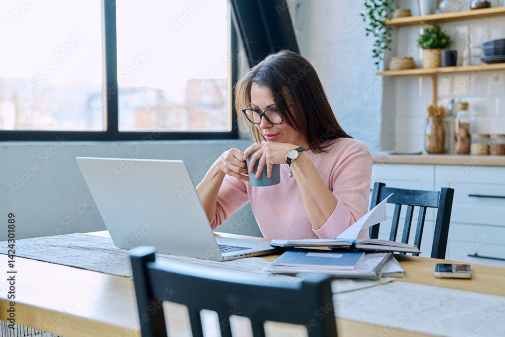 Middle aged woman working with laptop sitting at table at home
