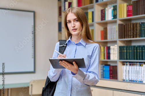 Portrait of student teenager girl using digital tablet inside classroom library