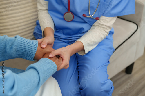 Asian female physical therapist wearing blue uniform holding elderly male patient's hand gently during home care session showing empathy support encouragement rehabilitation therapy relationship