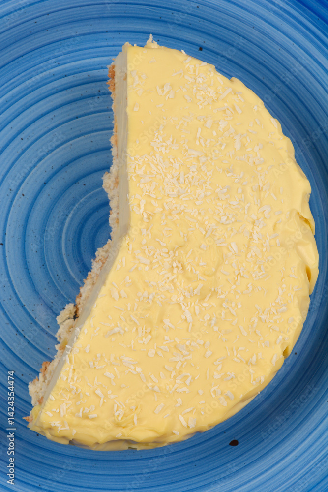 A partially eaten vanilla and coconut cake with a light yellow cream and coconut flakes sits on a textured blue plate