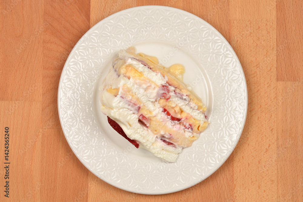 A slice of Frozen wind cake (layered meringue cake with whipped cream and fruit) is presented on a white ornate plate