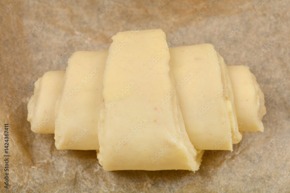 A single, unbaked croissant dough rests on a piece of parchment paper, ready for the oven