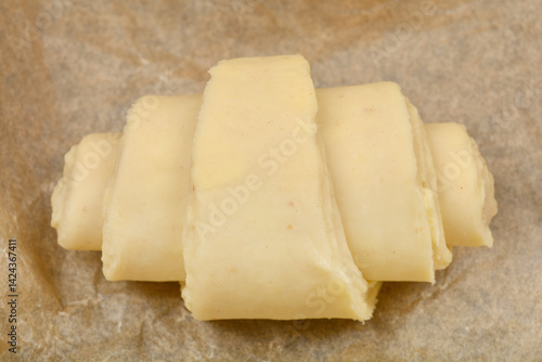 Obraz na płótnie A single, unbaked croissant dough rests on a piece of parchment paper, ready for the oven w salonie