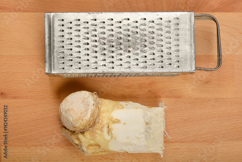Obraz na płótnie A piece of horseradish root is positioned below a meta grater on a light brown wooden board w salonie