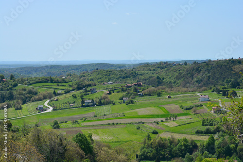 Obraz na płótnie A picturesque view from Gornje Psarjevo in Croatia extends eastward over lush green fields and scattered houses under a clear sky w salonie