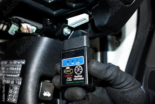 Obraz na płótnie OBD2 Scanner Tool, A gloved hand holds an OBD2 scanner, ready to connect to a car's diagnostic port for checking fault codes and real time information. Car diagnostics, auto repair tool. w salonie