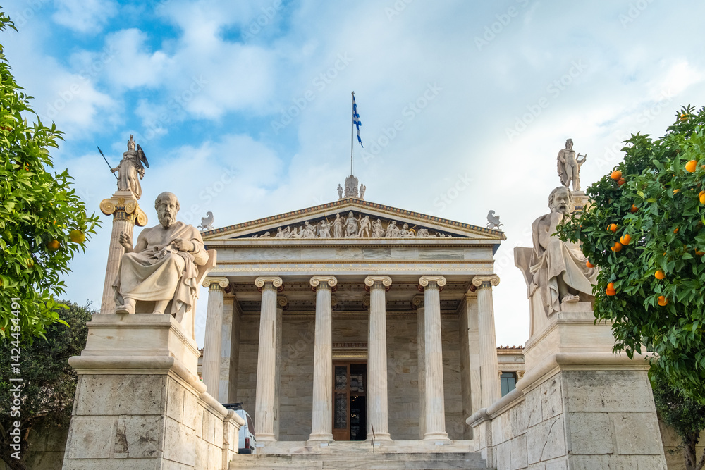 Fototapeta premium Academy of Athens with marble columns with sculptures of Apollo and Athena and tangerine trees in Athens, Greece. Popular landmark and travel destination