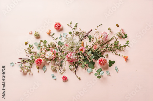 The image shows a beautiful arrangement of various flowers and greenery scattered on a pink background