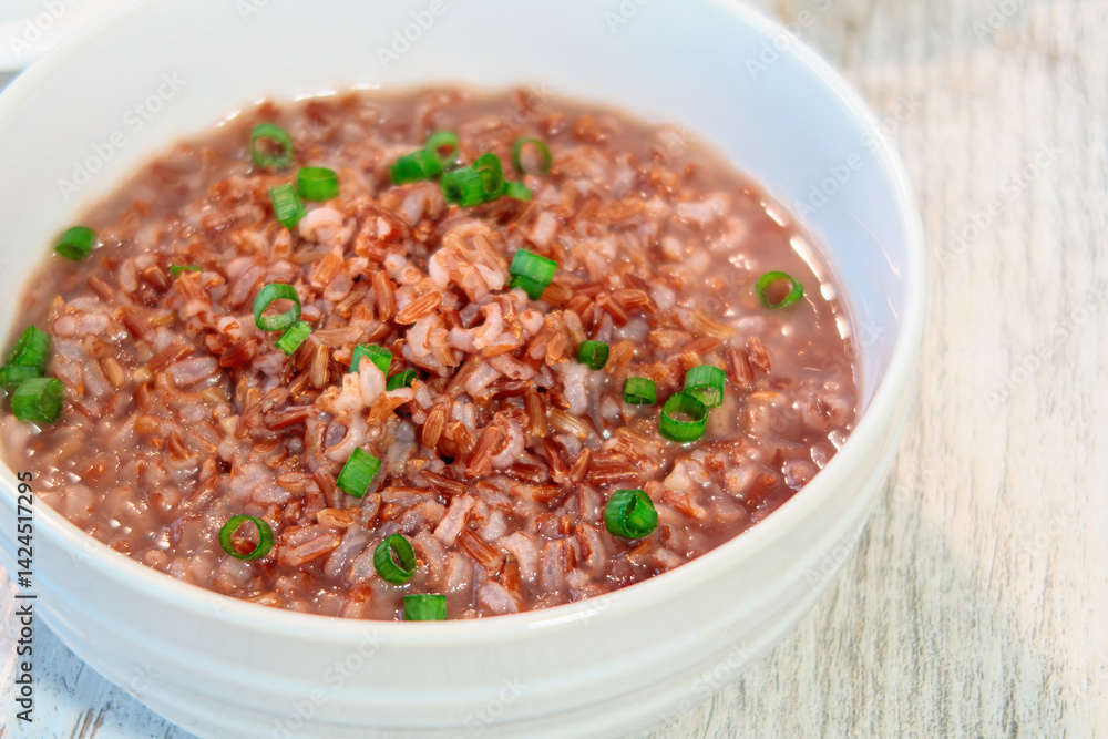 Close up of a bowl of brown rice porridge with chopped green onions on a white wooden surface, Healthy comfort food. Close up of a bowl of brown rice porridge with chopped green onions on a white wooden surface, Healthy comfort food.