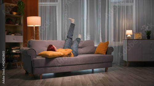 Redhead woman in casual clothes rest on the sofa in her apartment. Long shot. Slow motion
