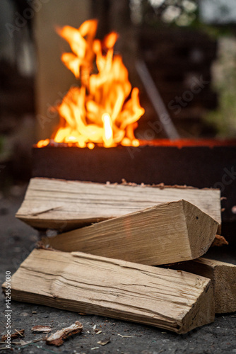 Burning wooden logs with hot flames of fire. Firewood burning on barbecue. Open fire. Birch firewood is lying nearby.