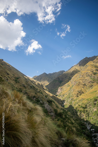 Golden hour mountain scene with sunlight hitting the slopes and blue sky with dramatic clouds. A scenic outdoor view conveying serenity and elevation. Perfect for adventure or ecotourism concepts.