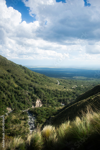 Mountain valley view with a winding road stretching through lush green hills. Captured from a high vantage point under a moody sky. A peaceful natural landscape ideal for travel and nature themes.